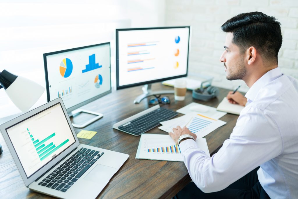 Confident handsome male freelance salesman analyzing data from screen at desk Estratégia Digital